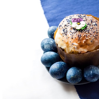 Gâteau de pâques décoré de fleur de sucre et d'œufs de couleur bleue sur une assiette sur fond de tissu blanc et bleu avec espace de copie. les œufs étaient colorés en bleu avec une décoction d'hibiscus