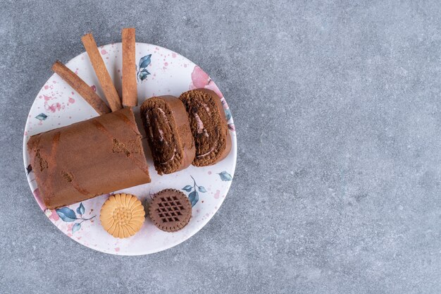 Gâteau roulé au chocolat, biscuits et bâtons de cannelle sur une assiette colorée