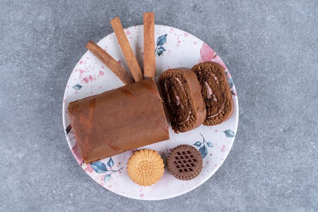 Gâteau roulé au chocolat, biscuits et bâtons de cannelle sur une assiette colorée