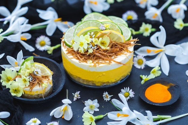 Gâteau végétalien cru au citron et citron vert sur une surface noire recouverte de petites fleurs de marguerite