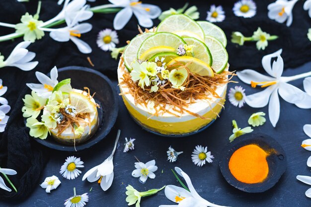 Gâteau végétalien cru au citron et citron vert sur une surface noire recouverte de petites fleurs de marguerite