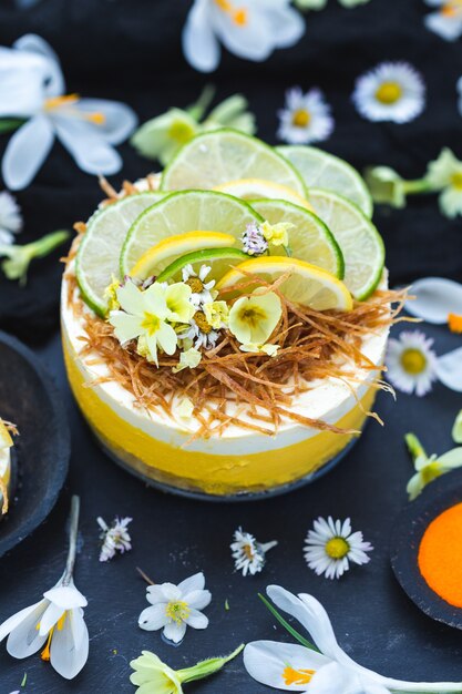Gâteau végétalien cru au citron et citron vert sur une surface noire recouverte de petites fleurs de marguerite