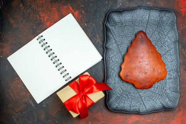 Gâteau vue de dessus sur un plateau noir cadeau attaché avec un carnet de ruban rouge sur une table rouge foncé