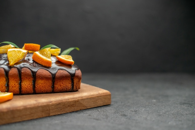 Photo gratuite gâteaux mous sur une planche à découper et couper les oranges avec des feuilles sur table sombre