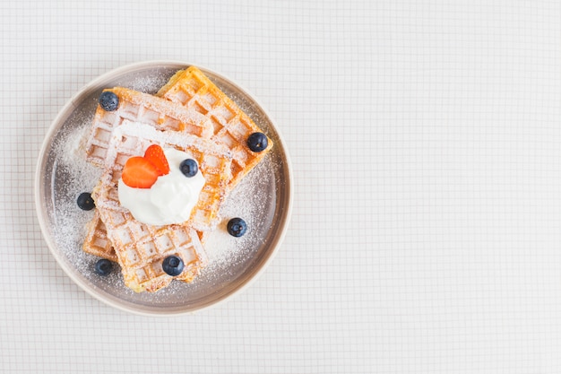 Gaufre brune dorée garnie de fraises tranchées; myrtilles et crème fouettée sur plaque