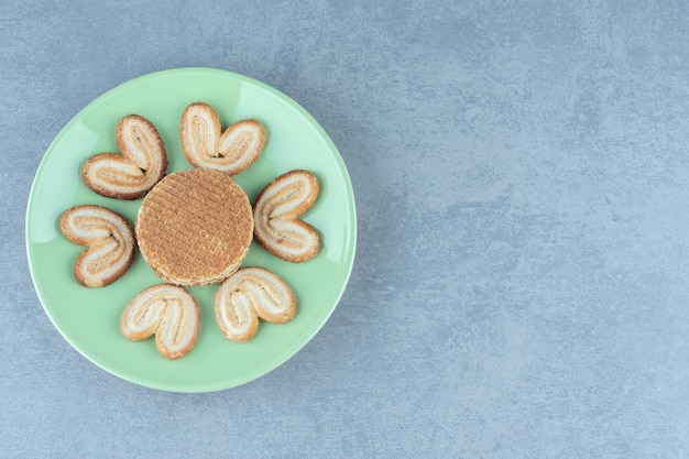 Gaufres et cookies sur plaque verte sur gris.