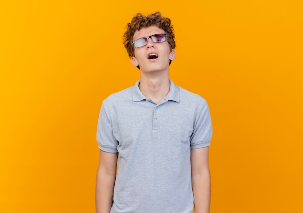 Gêné Jeune Homme à Lunettes Noires Portant Un Polo Gris Criant Avec Une Expression Agacée Sur Orange