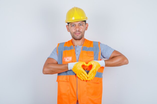 Générateur de sexe masculin montrant le symbole du cœur et la forme avec les mains en uniforme et à la vue de face, heureux.