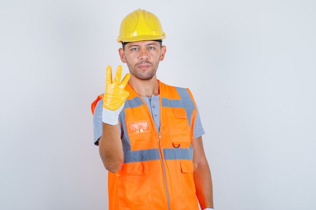 Générateur de sexe masculin en uniforme pointant vers le haut avec les doigts numéro trois, vue de face.