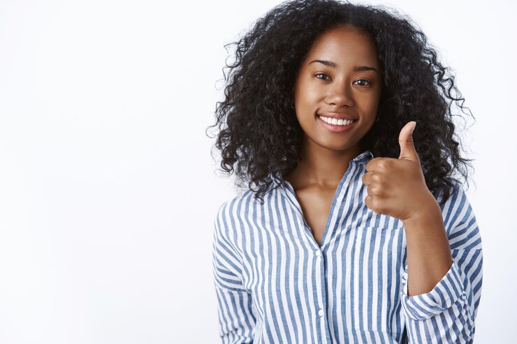 Photo gratuit génial bien fait. amie à la peau foncée satisfaite et satisfaite portant un chemisier rayé souriant affirmatif montrant le pouce vers le haut comme approuver votre idée, souriant mur blanc satisfait