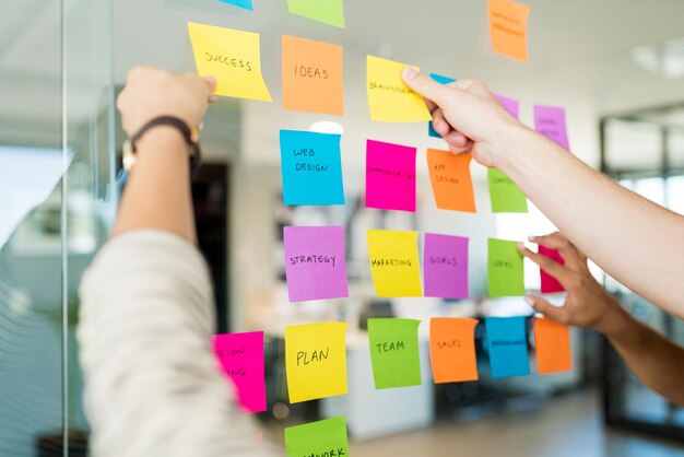 Gens d'affaires organisant diverses notes adhésives avec du texte sur du verre au bureau