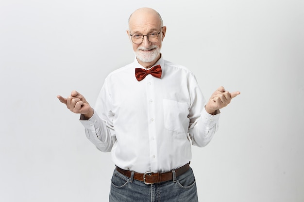 Les gens, l'âge mûr, la retraite et le concept de sagesse. Photo de bel homme européen âgé gai avec une barbe grise épaisse pointant l'index dans des directions opposées et souriant de manière ludique