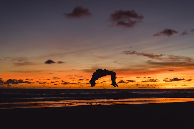 les gens au bord de l&#39;océan au coucher du soleil. l&#39;homme saute sur le fond du soleil couchant
