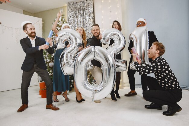 Les gens dans une décoration de Noël. Homme en costume noir. Célébrations de groupe Nouvel an. Les gens avec des ballons 2021.