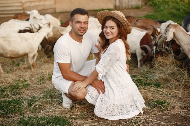 Les gens dans une ferme. Accoupler avec une chèvre. Femme en robe blanche.