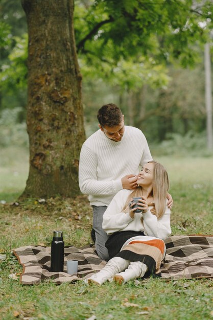 Les gens dans un parc. Femme en manteau marron. Homme dans un pull blanc. Couple dans un pique-nique.