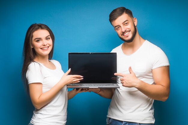 Des gens heureux tout en tenant un ordinateur portable noir isolé sur bleu