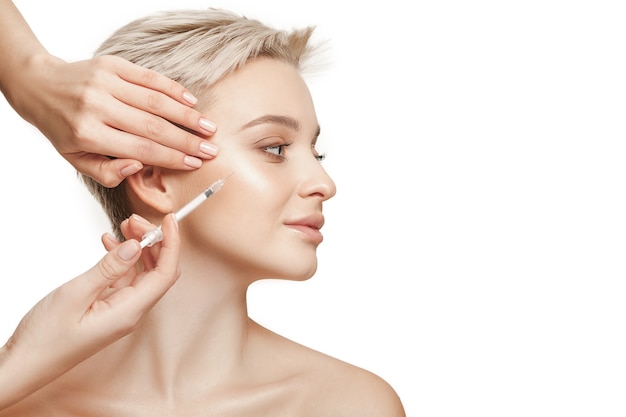 Les gens, les lèvres, la cosmétologie, la chirurgie plastique et le concept de beauté - beau visage de jeune femme et main avec une seringue faisant l'injection