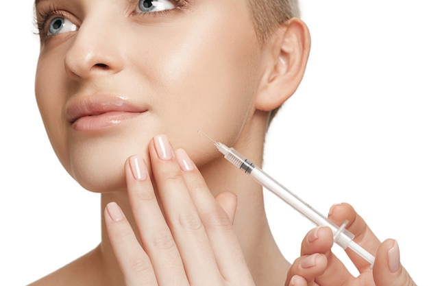 Les gens, les lèvres, la cosmétologie, la chirurgie plastique et le concept de beauté - beau visage de jeune femme et main avec une seringue faisant l'injection