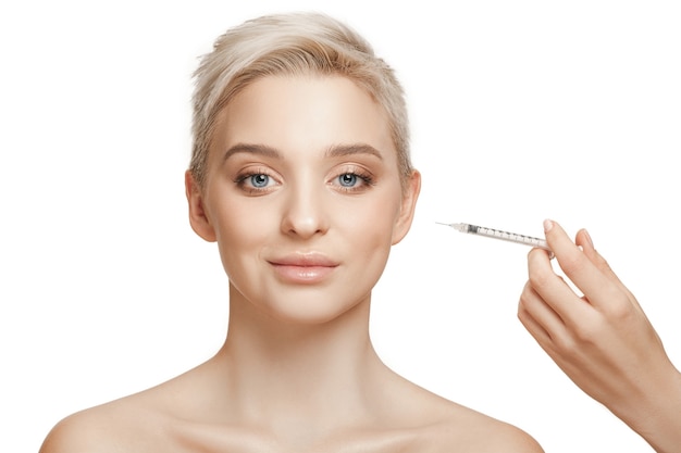 Les gens, les lèvres, la cosmétologie, la chirurgie plastique et le concept de beauté - le visage et la main d'une belle jeune femme avec une seringue faisant l'injection