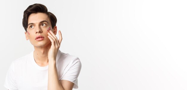 Les gens lgbtq communauté et concept de style de vie Beau jeune homme gay appliquant des paillettes sous les yeux pour la fête de la fierté debout sur fond blanc