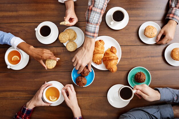 les gens les mains sur la table en bois avec des croissants et du café.