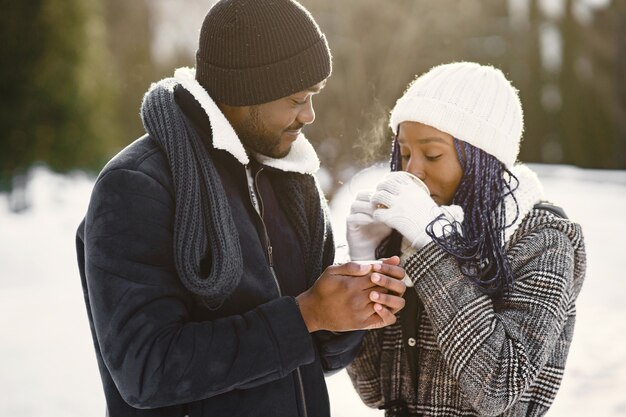 Les gens marchent dehors. Jour d'hiver. Couple africain avec café.