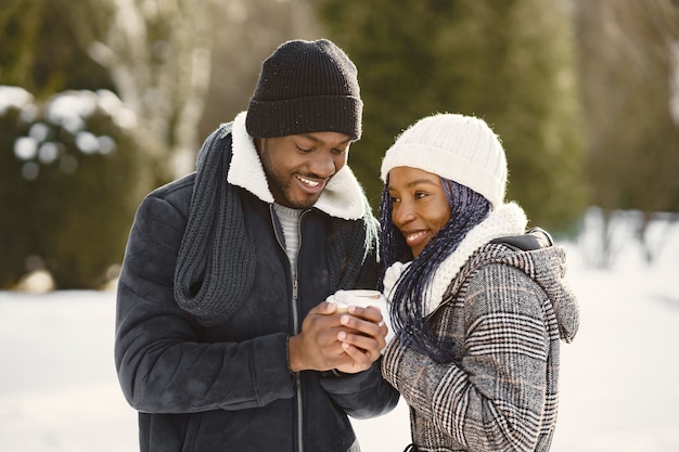 Les gens marchent dehors. Jour d'hiver. Couple africain avec café.