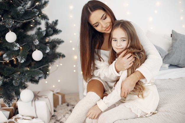 Les gens se préparent pour Noël. Mère jouant avec sa fille. Famille assise sur un lit. Petite fille en robe blanche.