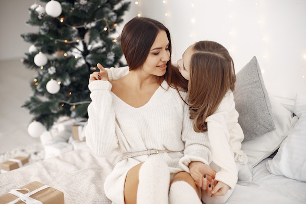 Les gens se préparent pour Noël. Mère jouant avec sa fille. Famille assise sur un lit. Petite fille en robe blanche.