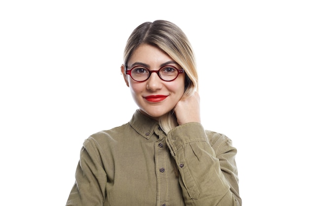 Les gens, le style de vie, la beauté, la mode et le style. Jeune femme européenne à la mode portant des lunettes à la mode, rouge à lèvres et chemise élégante posant au mur blanc avec une expression faciale excitée heureuse