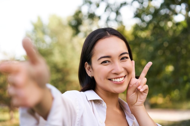 Les gens et le style de vie une femme asiatique heureuse prend un selfie dans une photo de parc sur un smartphone en souriant et en regardant