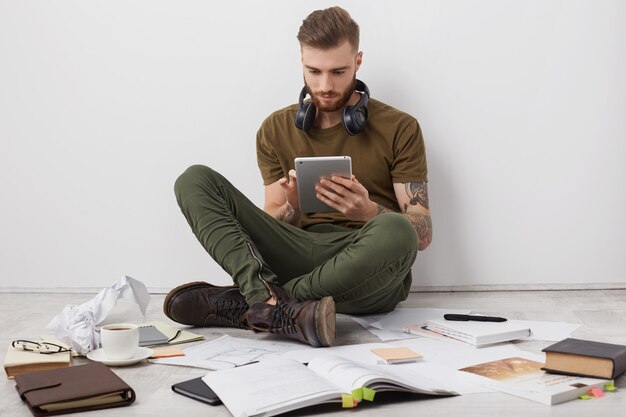 Les gens, la technologie moderne et le concept de l'éducation. Homme élégant barbu porte des bottes, est assis les jambes croisées sur le sol,