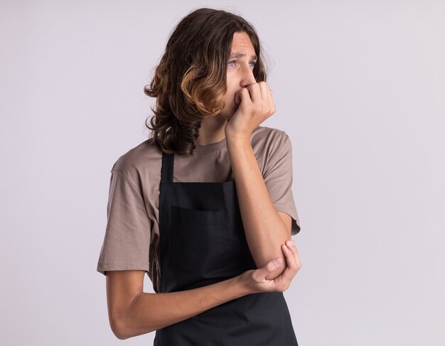 Gentil jeune beau barbier portant l'uniforme mettant la main sur la bouche regardant le côté isolé sur un mur blanc avec espace de copie