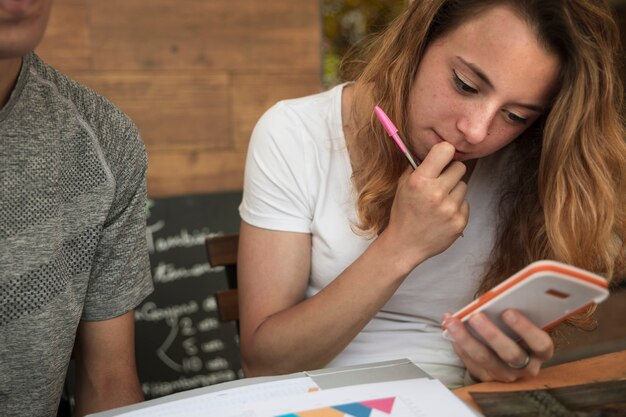 Gentil jeune blonde à l&#39;aide de la calculatrice près de diagrammes sur papier