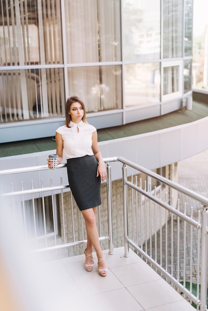 Gentil jeune femme d&#39;affaires tenant une tasse de café à emporter debout sur le balcon