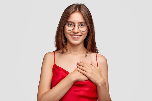 Gentil sympathique jeune femme brune posant contre le mur blanc