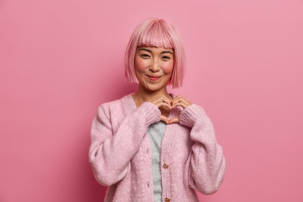 Gentille femme asiatique aimable positive avec une coiffure bob, fait un geste en forme de coeur