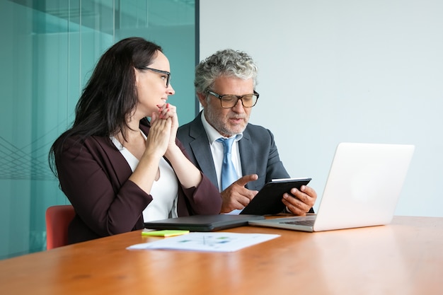 Gestionnaire et exécutif discutant du projet. Collègues réunis à table avec un ordinateur portable ouvert, utilisant une tablette et parlant.