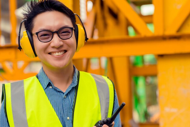 Gestionnaire d'ingénieur asiatique intelligent avec uniforme de sécurité vérifiant la construction du site avec fond de structure en acier et en béton