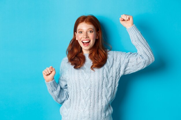 Gil rousse gai gagnant, célébrant la victoire, souriant et sautant du bonheur, posant sur fond bleu.