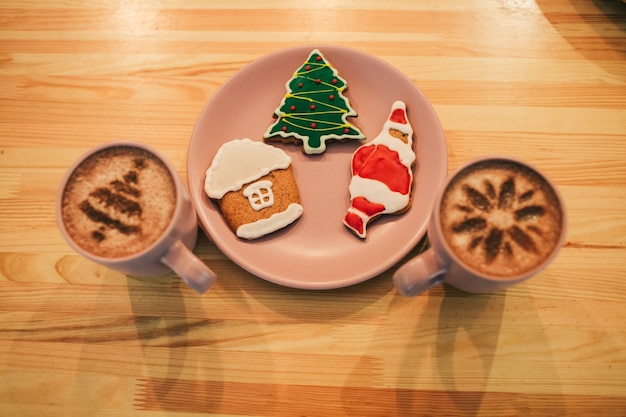 Gingerbreads with Christmas design se trouvent sur une assiette rose entre des tasses avec du café