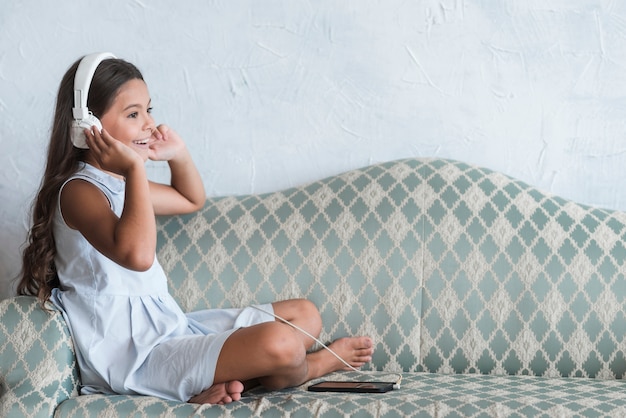 A, girl, séance, sofa, écoute, musique, sur, casque, attaché, a, téléphone portable