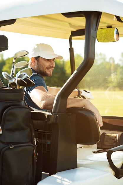 Golfeur masculin souriant assis dans une voiturette de golf