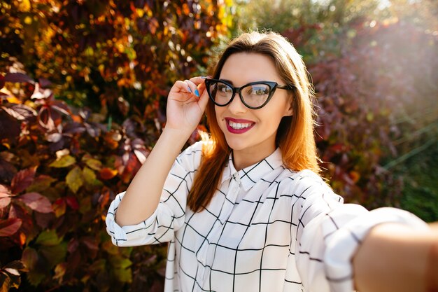 Gougeus modèle prend selfie tout en tenant ses lunettes d&#39;une main dans le jardin d&#39;automne.