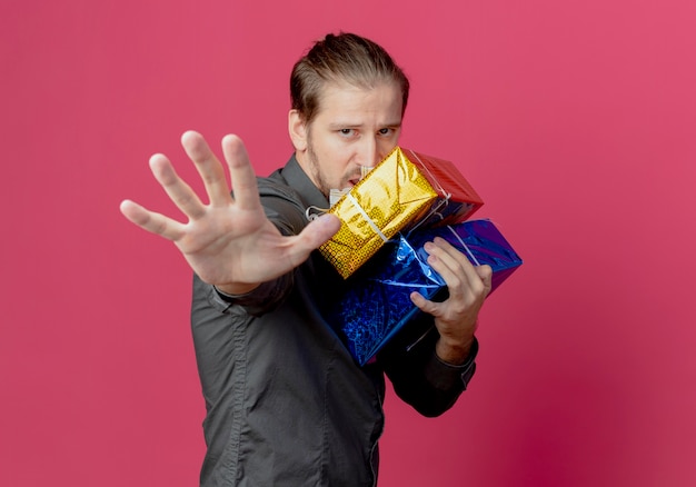 Gourmand bel homme se tient sur le côté tenant des coffrets cadeaux gestes stop main signe isolé sur mur rose