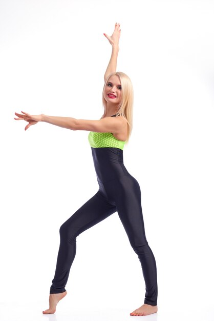 Grâce du sportif. Photo de toute la longueur d'une belle gymnaste blonde souriante posant joyeusement dans son survêtement slim sur fond blanc