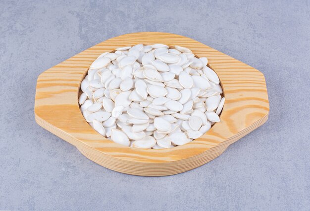 Graines de citrouille dans une assiette en bois sur marbre.