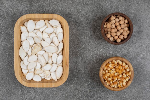 Graines de citrouille savoureuses, grains de maïs et pois sur marbre.