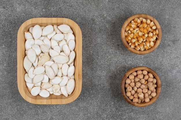 Graines de citrouille savoureuses, grains de maïs et pois sur marbre.